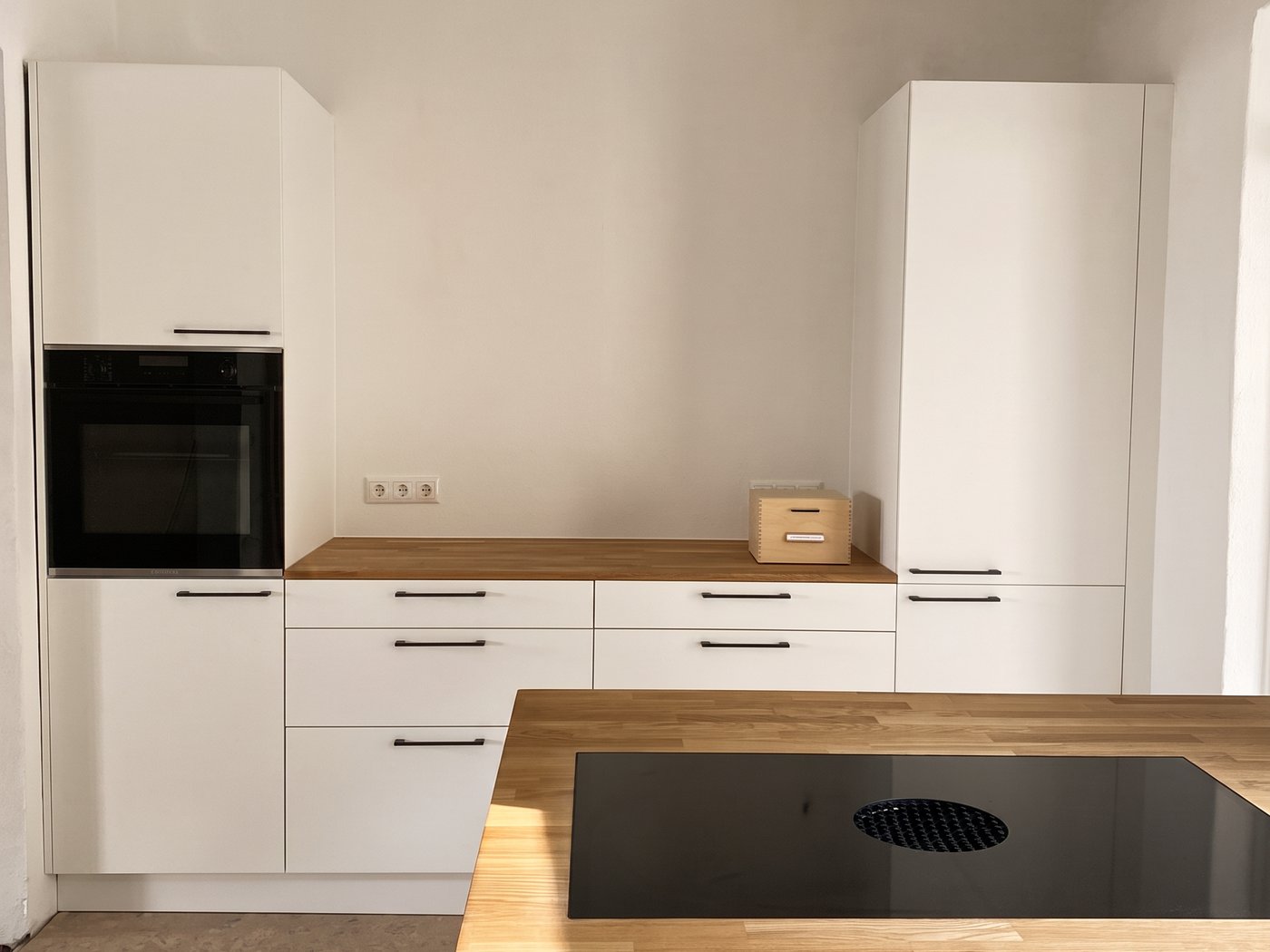 Weiße Küchenzeile mit Backofen im Hochschrank und durchlaufender Eichenarbeitsplatte